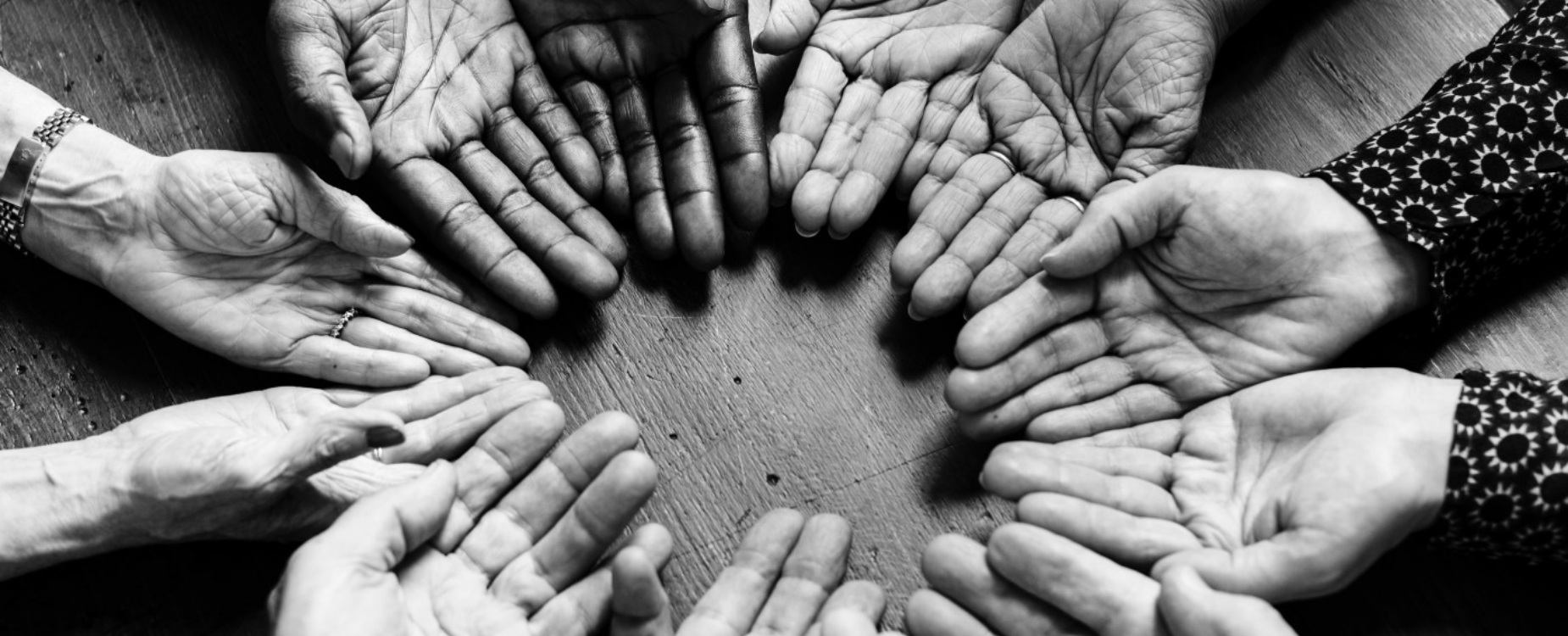 Several open hands arranged in a circle over a table, symbolising community, inclusion and support.